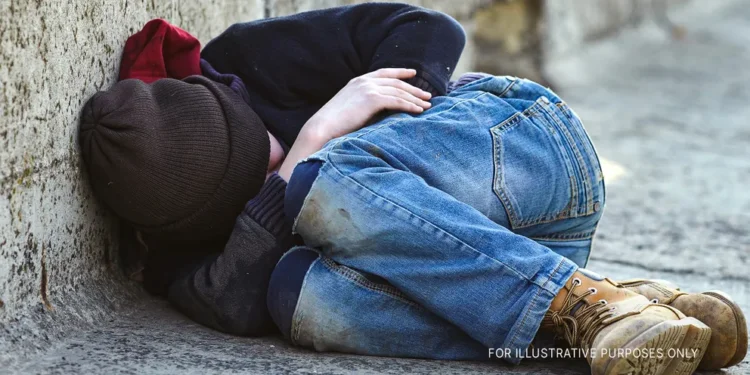 A young boy curled up while sleeping on the street | Source: Shutterstock